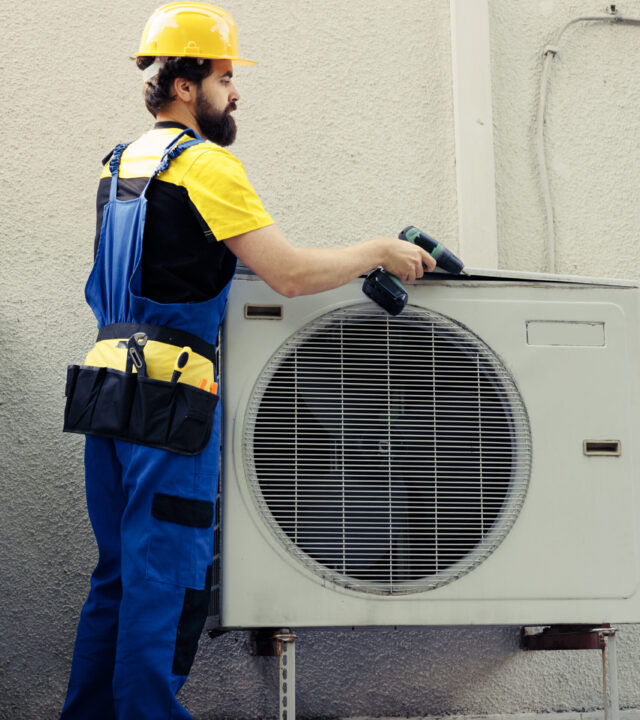 Technician working on air conditioner Professional technician starting work on faulty air conditioner, using power drill to disassemble condenser metal coil panel. Expert engineer dismantling hvac system to check for leaks