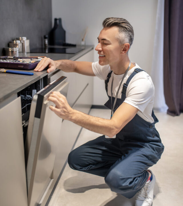 Man crouched peeking into crack door of washing machine Dishwasher Use Tips for Better Performance