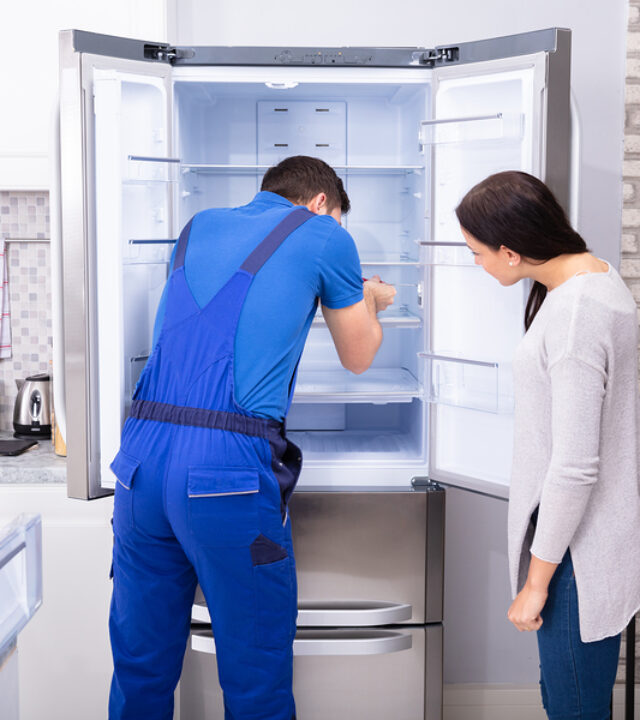 Woman Looking At Male Repairman Fixing Refrigerator With Screwdr The Benefits of Prompt Freezer Repair